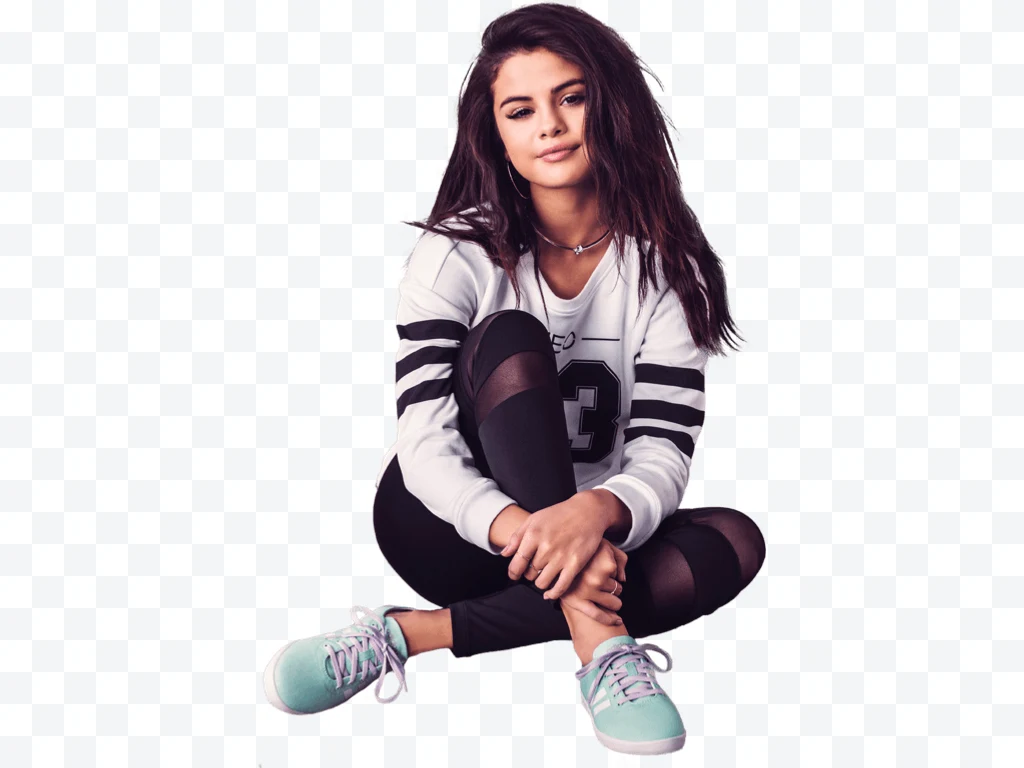 Selena Gomez sitting in black and white sportswear and green sneakers.