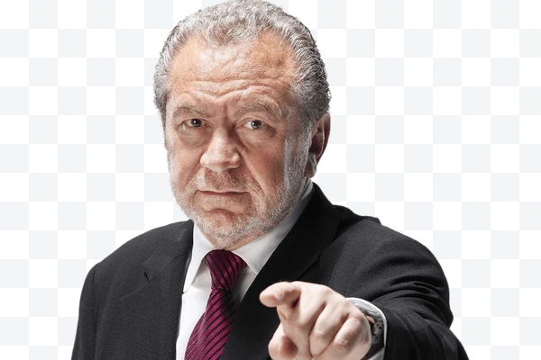 Lord Alan Sugar con traje negro y corbata roja señalando hacia adelante