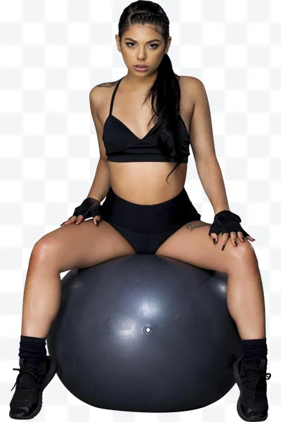 Mujer joven con ropa deportiva negra sentada sobre una pelota de ejercicio gris.
